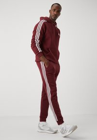 adidas Sportswear ESSENTIALS TAPERED CUFF 3-STRIPES  - Treniņtērpa apakšdaļas - shadow red
