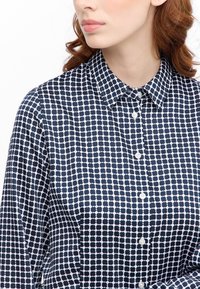 Camicia a polo blu navy e bianca con un colletto button-down, caratterizzata da un design a pois floreali e da una texture di tessuto liscia.
