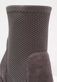 Szare botki za kostkę z teksturowanym górnym materiałem z dzianiny oraz gładkim zamszowym panelem. Projekt obejmuje dopasowany krój z zaokrąglonym brzegiem na górze.