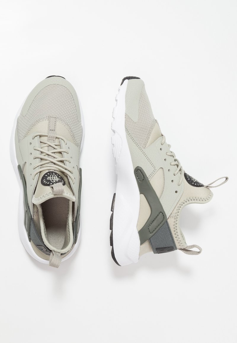 Paire de baskets athlétiques gris clair avec semelles blanches et accents gris foncé, vues de dessus et de côté sur fond blanc.