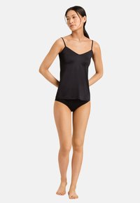 Camisola nera in satin con spalline sottili e scollatura a scallop, abbinata a un bikini bottom nero, che mette in mostra una texture liscia e un design classico.