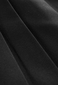 Sort stof med en glat, tekstureret overflade, der har diagonale folder og et ensartet vævemønster. Velegnet til beklædning eller polstring.