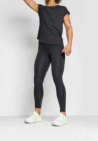 Camiseta atlética negra de manga corta, combinada con leggings negros con cremalleras laterales, llevada con zapatillas blancas con detalles en verde.