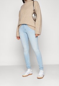 Jeans skinny de color azul claro combinados con un suéter grande de color beige y zapatillas blancas. El suéter tiene un cuello alto y puños acanalados.