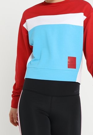 Persoon draagt een color-blocked sweatshirt met rode mouwen, een witte en blauwe voorkant, en zwarte legging met zijstrepen.