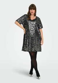 Juoda ir sidabrinė leopardų rašto suknelė su laisvu fasonu, trumpomis rankovėmis ir V formos iškirpte, derinama su juodomis tamprėmis ir sidabriškais kulnais.