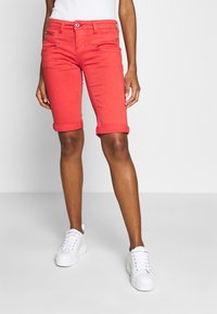 Punaiset farkkushortsit, joissa on kapea istuvuus, käännetyt lahkeet ja etutaskut. Yhdistetty valkoisiin tennareihin. Tasainen muotoilu ja sileä tekstuuri.