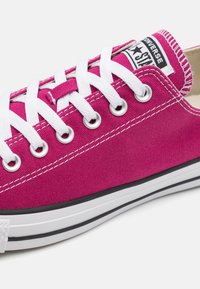 Różowe trampki z płótna z białymi sznurowadłami i oczkami, z czarno-białą gumową podeszwą, logiem na języku i białymi detalami szwów.