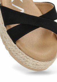 Sandalias de plataforma con tiras cruzadas negras, con una suela de esparto texturizada natural y una plantilla beige suave. Cuenta con una suela de goma para mayor agarre.