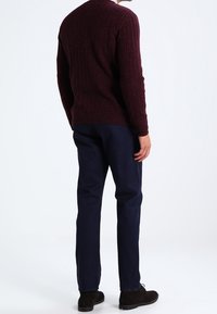 Viininpunainen neulepaita, jossa on teksturoitu kuvio, yhdistetty tummansinisiin housuihin. Malli pukeutuneena tummiin kenkiin, nähtynä takaa.