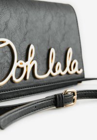 Črna usnjena torbica z zlatim napisom "Ooh la la" in odstranljivim trakom z zlatim kovinskim detajli. Teksturovana površina.