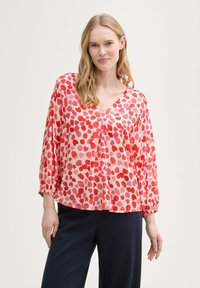 Blusa pattern rossa e rosa con scollatura a V, maniche lunghe e polsi elasticizzati, realizzata in tessuto leggero e semitrasparente.
