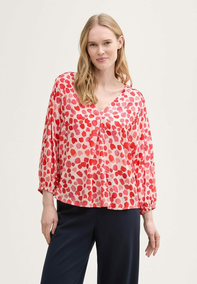 Blusa pattern rossa e rosa con scollatura a V, maniche lunghe e polsi elasticizzati, realizzata in tessuto leggero e semitrasparente.