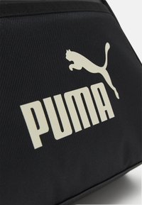 Schwarze Stofftasche mit einem auffälligen weißen "PUMA"-Logo und einem springenden Puma-Motiv. Die Textur ist glatt mit einem leicht gerippten Muster.