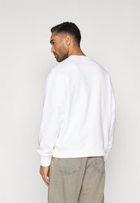 Λευκό φούτερ με στρογγυλή λαιμόκοψη, ριμπ μανσέτες και τελείωμα. Το ύφασμα φαίνεται απαλό με ομαλή υφή και έχει στυλ με άνετο τζιν παντελόνι.