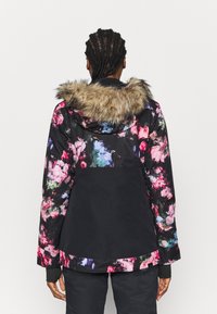 Giacca nera con motivo floreale e cappuccio foderato in pelliccia. Presenta una chiusura con cerniera e polsini elasticizzati, con dettagli luminosi in rosa e verde.