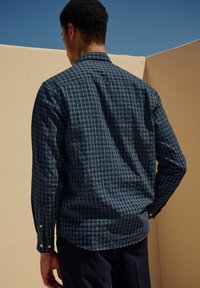 Blauwe geruite shirt met een button-down kraag, gemaakt van zachte stof, met lange mouwen en witte knopen, gezien vanaf de achterkant.