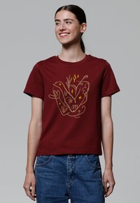 T-shirt en coton bourgogne avec un design graphique doré intégrant des éléments floraux et des étoiles. Manches courtes et encolure classique.