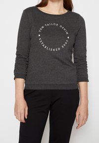Felpa grigia a maniche lunghe con scollatura rotonda, caratterizzata da un logo circolare bianco che include la scritta "Tom Tailor Denim Established 2007."