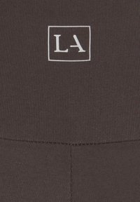 Svart ribbad tyg med en vit rektangulär logotyp med bokstäverna "LA" i mitten. Texturen är slät med synliga sömmar.