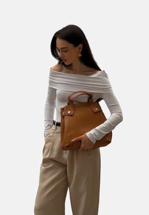 Borsa a mano in pelle marrone con due manici corti, dettagli in metallo argentato e forma strutturata, abbinata a un top bianco scollato sulle spalle e pantaloni beige.