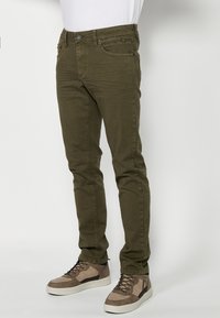 Jeans verde oliva de corte slim, confeccionados en denim, que cuentan con bolsillos delanteros, cierre de botón y detalles de costura a lo largo de las piernas.