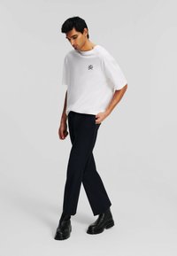 T-shirt bianco a maniche corte con dettagli ricamati neri, abbinato a pantaloni blu scuro e stivali neri chunky. Tessuto morbido.