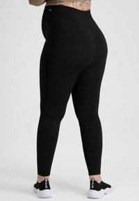 Zwarte geribde leggings met een hoge tailleband, een gladde textuur en een strakke pasvorm, gecombineerd met zwarte sportieve schoenen met logo-accenten.