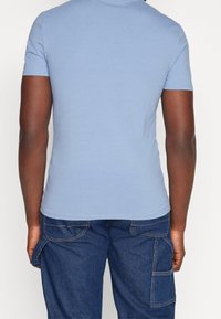 Lyseblå, kortærmet, crew neck t-shirt; glat tekstur; tætsiddende snit; parret med mørkeblå cargo bukser med sidelommer.