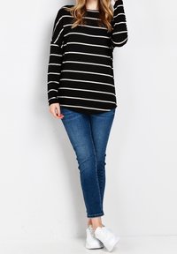 Czarna i biała w pionowe paski koszula z długim rękawem z zaokrąglonym dołem, w połączeniu z niebieskimi dżinsami i białymi sneakersami. Teksturowana tkanina, luźny krój.