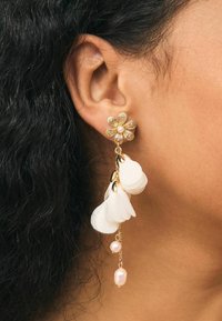 Gold-tone earrings feature a floral design with a central pearl, dangling white petal accents, and pink pearl drops. Textured and delicate.