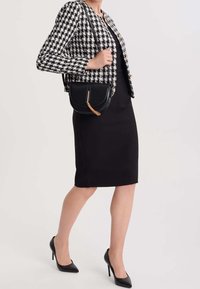 Černobílý houndstooth kabát, černé šaty a černá crossbody taška se zlatými akcenty. Modelka má na sobě černé vysoké podpatky.