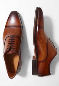 Chaussures habillées en cuir marron avec une finition polie, bout carré, cinq œillets, et un talon empilé. Les lacets sont assortis à la couleur des chaussures.
