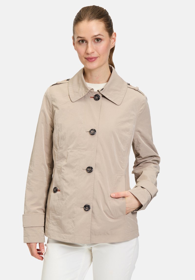 Helle beige Trenchcoat mit Kragen, sechs schwarzen Knöpfen, Seitentaschen und geknöpften Schulterklappen. Glatte Textur.