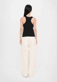 Black sleeveless tank top features a racerback design. Paired with cream wide-leg pants, showing back view and minimal detailing.
