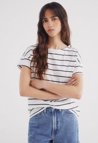 White short-sleeve top with navy stripes, round neckline with button details, paired with high-waisted blue denim shorts.