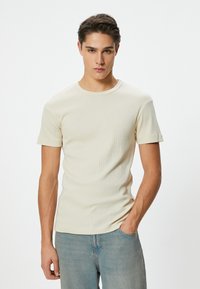 Beige ribbet t-shirt med korte ærmer og rund halsudskæring, med en tætsiddende pasform og en glat tekstur, parret med lyseblå jeans.
