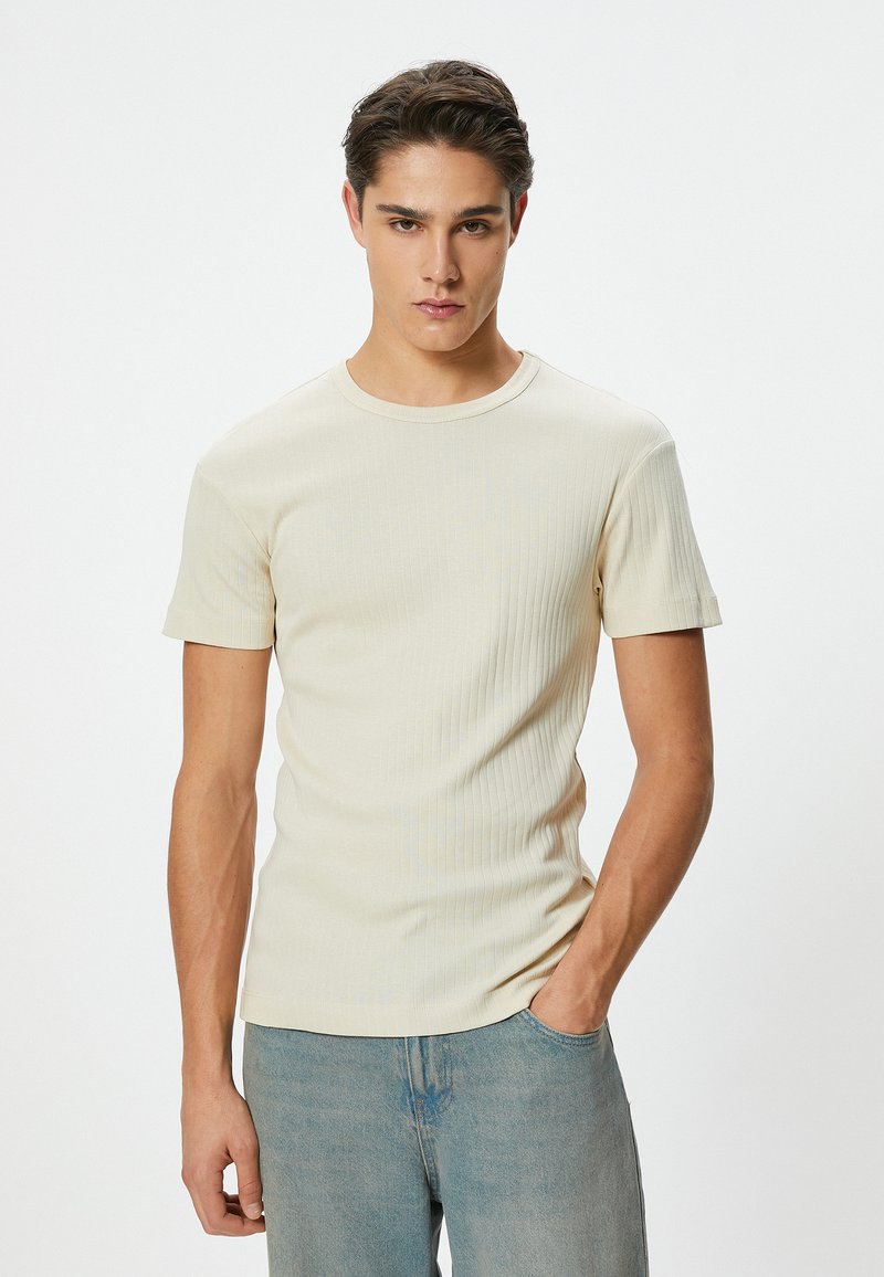 Beige ribbet t-shirt med korte ærmer og rund halsudskæring, med en tætsiddende pasform og en glat tekstur, parret med lyseblå jeans.