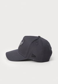 Tumši zila beisbola cepure ar izliekto vizieri, kurai priekšā ir izteiksmīgs izšūts logotips un mazs logotipa etiketē sānos.