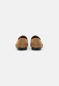 Scarpe marroni in suede con una texture liscia, forma arrotondata e un design minimalista. La scarpa presenta un tacco basso e una suola solida.