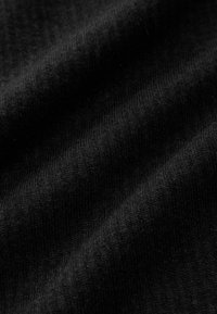 Des rideaux en tissu noir avec une texture douce et lisse ; affichent de fins motifs de tricot et des nuances variées de noir sous la lumière et l'ombre.