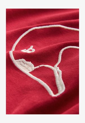 Roter Stoff mit erhabenem weißen Stickmuster eines stilisierten Grafiks, das eine glatte Textur und klare Linien vor dem Hintergrund hervorhebt.