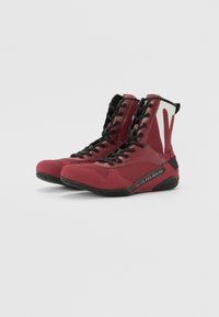 Scarpe da boxe alte rosse con tomaia in rete, lacci neri e suola testurizzata, con branding sul tallone e dettagli di accento.