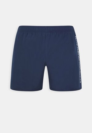 Bañadores de color azul marino en un material ligero, con una cintura elástica y un logo impreso en el costado. Diseño simple y textura suave.