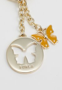 Zlatno-metalni privjesak s izrezbarenim motivom leptira i ugraviranim natpisom "FURLA", ukrašen žutom emajliranom leptiricom na lancu.