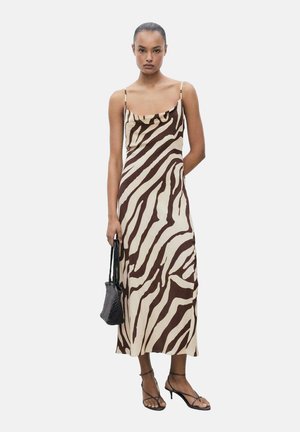 Vestido midi a rayas de cebra en marrón y crema con tirantes finos, un escote con volantes y un corte holgado. Combinado con sandalias negras y un bolso.