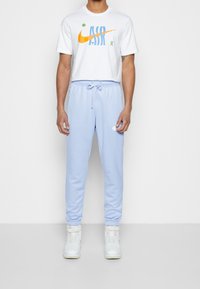 Bílé tričko s barevným logem Nike, doplněné o světle modré tepláky s elastickým pasem a bočními kapsami. Bílé tenisky.