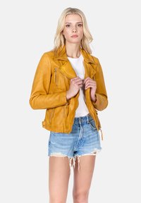 Žlutá kožená motorkářská bunda s diagonálním zipem, předními kapsami a širokými klopami. Nositá přes bílé tričko a kombinovaná s vybroušenými džíny šortkami.