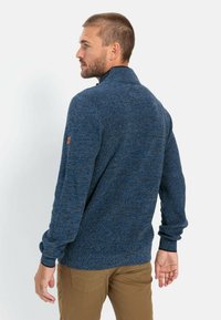 Knitted blue sweater with a high collar, featuring textured fabric and ribbed cuffs. Small logo detail on the left sleeve.