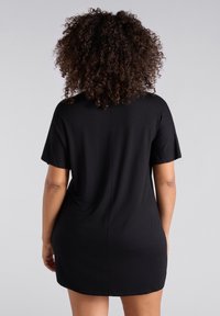 Vestido negro de manga corta, hecho de una tela suave y elástica, con un ajuste relajado y dobladillo redondeado, que presenta un sencillo detalle de costura en la parte posterior.